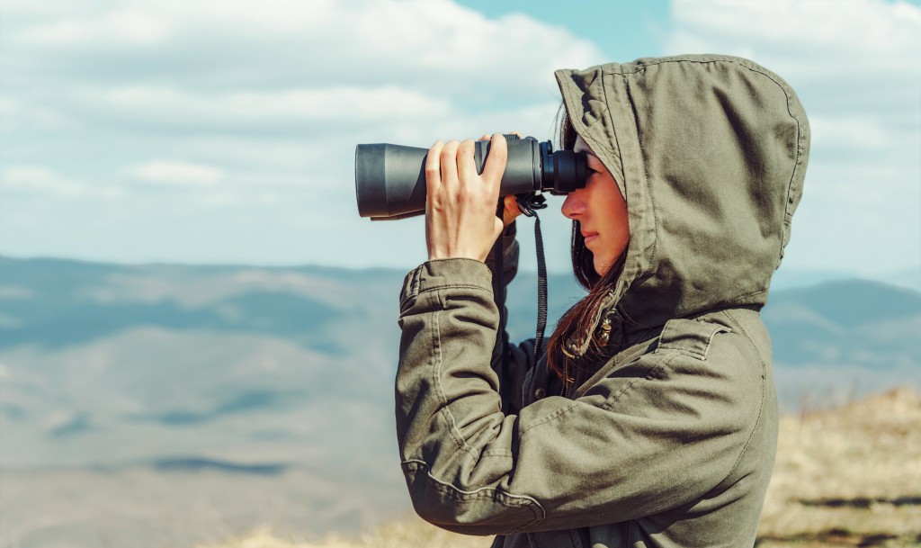 Hiker woman looking in binoculars in the mountains, side view